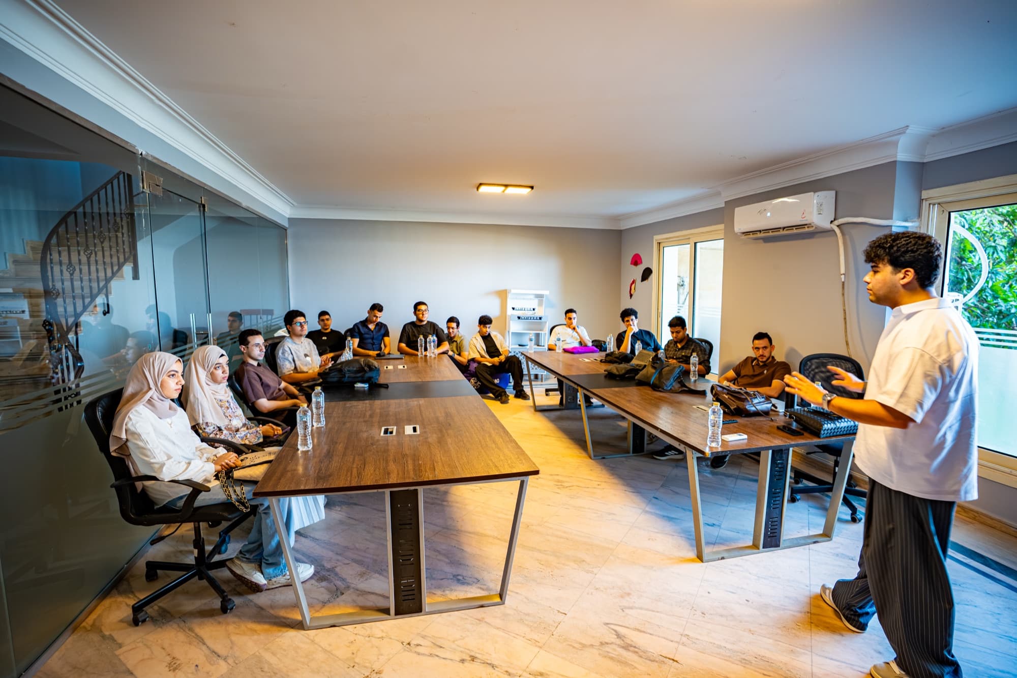 Anas Asfour speaking to a room of attendees seated around tables during a workshop